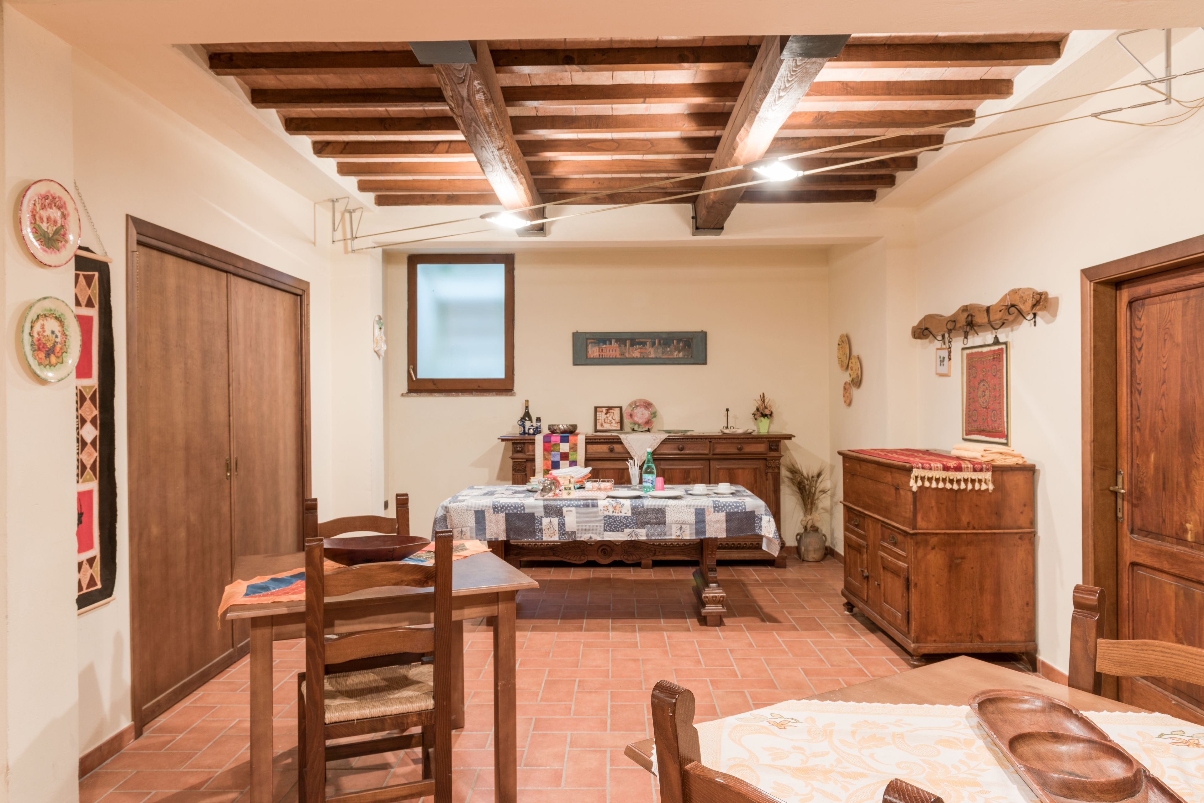 Un comedor con una mesa de madera, sillas y un banco. Se observa un armario de madera y una ventana al fondo.