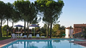Ein Pool mit Liegestühlen und Sonnenschirmen, umgeben von Bäumen und einem Gebäude.