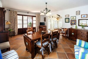 Un comedor con una mesa y sillas de madera, una araña y un televisor al fondo.