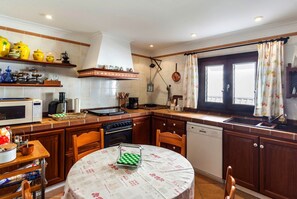Una cocina con una mesa redonda, armarios de madera, una estufa y una ventana con cortinas.