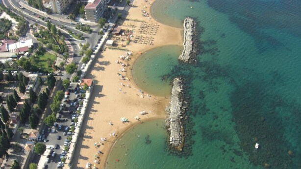 Vista aerea di una zona costiera con spiaggia, strada e affioramento roccioso.