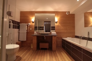 Un baño moderno con suelo de madera, una bañera grande, un lavabo con espejo y un inodoro.