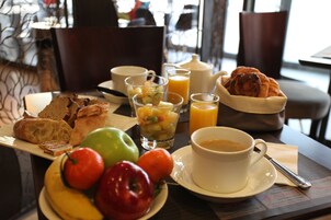 Un desayuno con pan, frutas, jugo y café sobre una mesa.