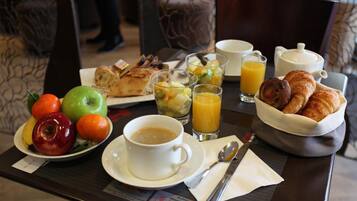 Een ontbijfwagen met croissants, fruit, sap, koffie en een theepot.