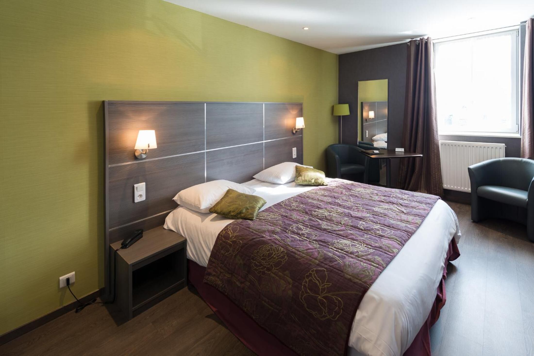 A hotel room with a large bed, bedside lamps, a desk with a chair, and a window with curtains.