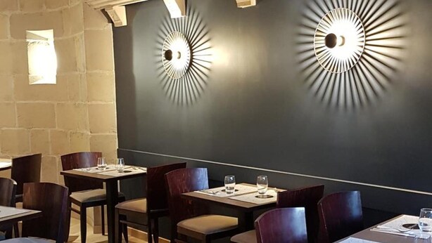 Ein Restaurant mit Holztischen und -stühlen, zwei Wandleuchten und einer Steinwand.