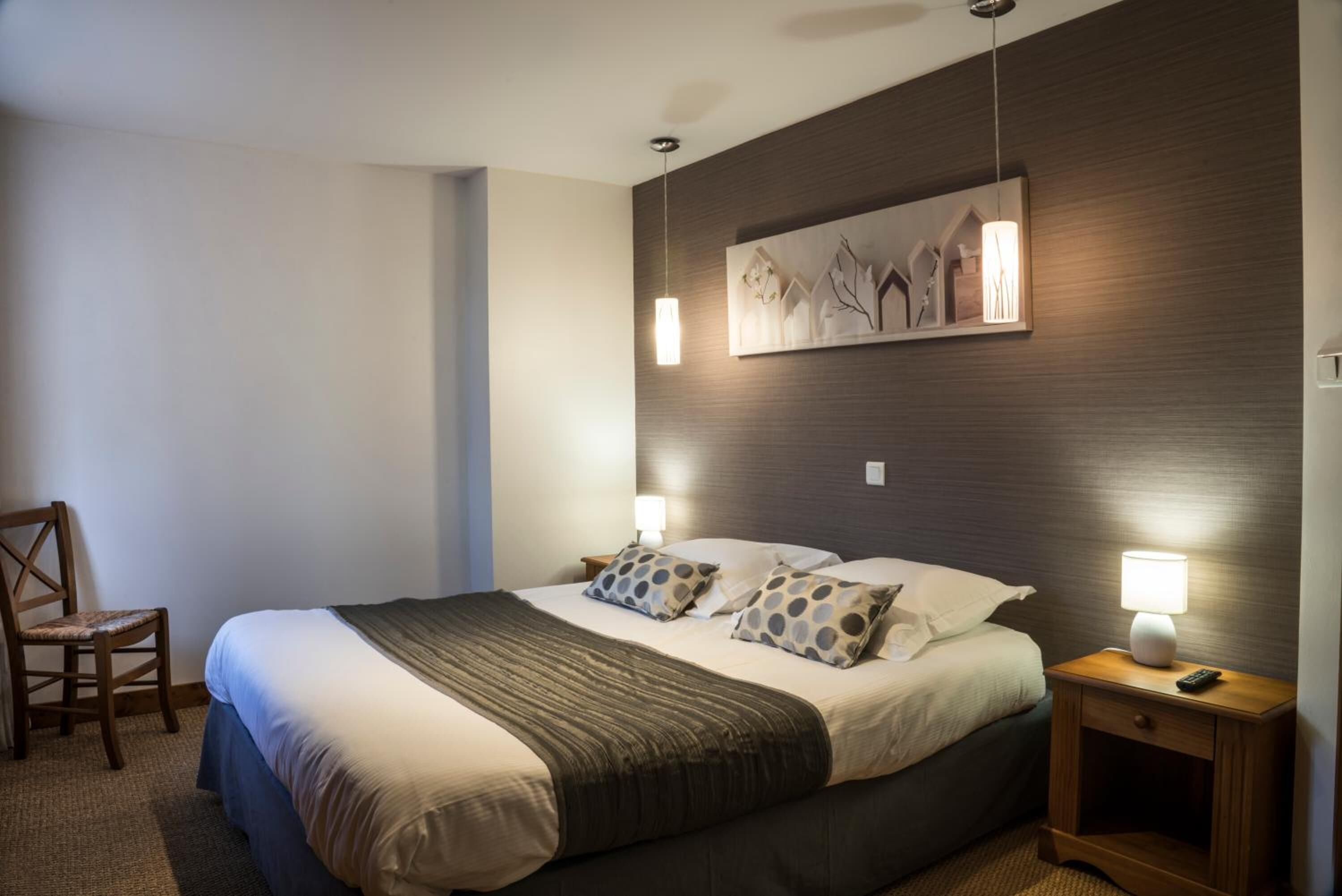 A neatly made bed with a dark headboard, two bedside lamps, and a wall-mounted artwork.