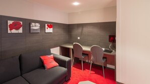 Ein modernes Zimmer mit grauem Sofa, roten Kissen, einem Schreibtisch, zwei Stühlen und einem roten Teppich.