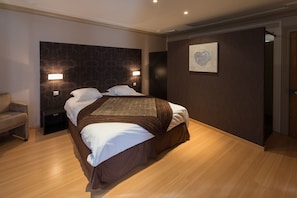 Un dormitorio moderno con una cama grande, dos mesitas de noche con lámparas, un cabecero oscuro estampado, suelo de madera y una obra de arte enmarcada en la pared.