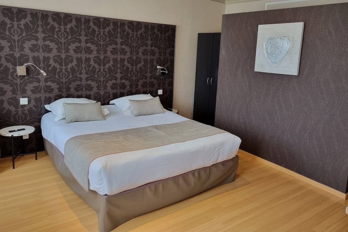 A neatly arranged bedroom with a large bed, a bedside table, a wall-mounted light, and a door.