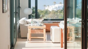 A modern room with a glass door, a sofa, a small table, and a view of palm trees and buildings.