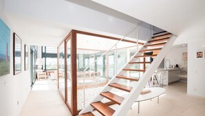 A modern interior with a wooden staircase, a glass door leading to a dining area, and a kitchen with white cabinets.