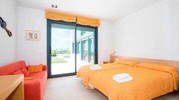 A bedroom with a bed, a red sofa, a wooden nightstand, and a large window with a view of a swimming pool.