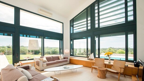 A spacious living room with large windows, a sofa, a coffee table, and a view of greenery and a pool.