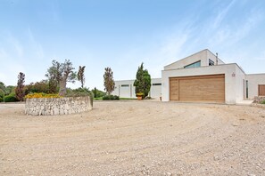 Un bâtiment moderne doté d’un grand garage, d’une allée en gravier et d’un mur en pierre agrémenté de plantes.