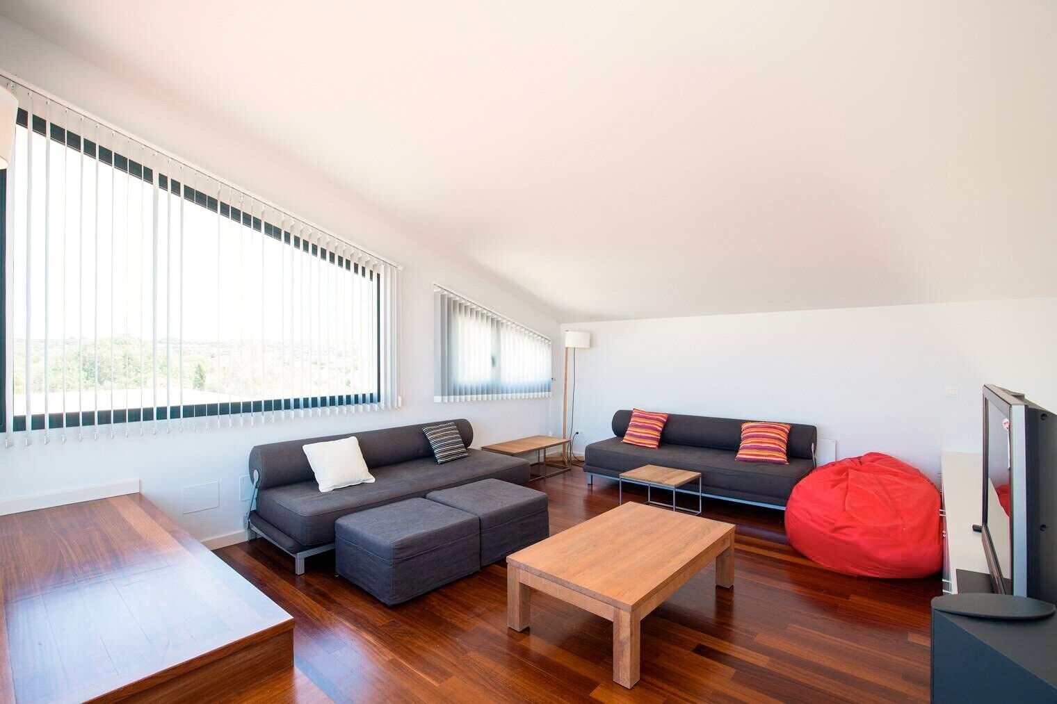 Una sala de estar moderna con un sofá, una mesa de centro, un sillón tipo petate rojo y un televisor.