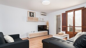 A modern living room with a flat-screen TV, a wooden cabinet, a black sofa, and a wooden coffee table. - Charming town house with pool - Casa Can Tatau (Santañyí)