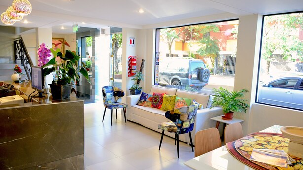 A modern hotel lobby with a reception desk, seating area, and large windows offering a view of the street. - Mandala Hotel (Encarnacion)