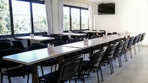 A conference room with long tables and chairs, large windows with curtains, and a flat-screen TV on the wall. - Mandala Hotel (Encarnacion)