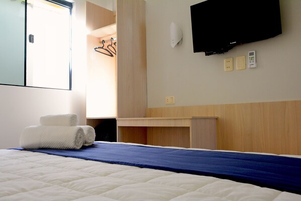 Una habitación de hotel con cama, escritorio, televisor y armario.