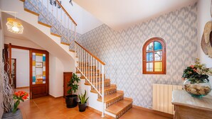 Un escalier avec des rampes blanches, un mur orné de motifs, une porte en bois et une fenêtre avec un vitrail décoratif.