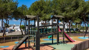Une aire de jeux avec des structures d’escalade et des toboggans, entourée d’arbres et d’une clôture.