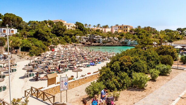 Une plage avec des parasols et des chaises longues, un mur de pierre et un panneau orné de symboles.