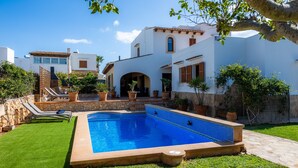 Une piscine bordée de pierres, une pelouse verdoyante et un bâtiment blanc avec un toit en tuiles.
