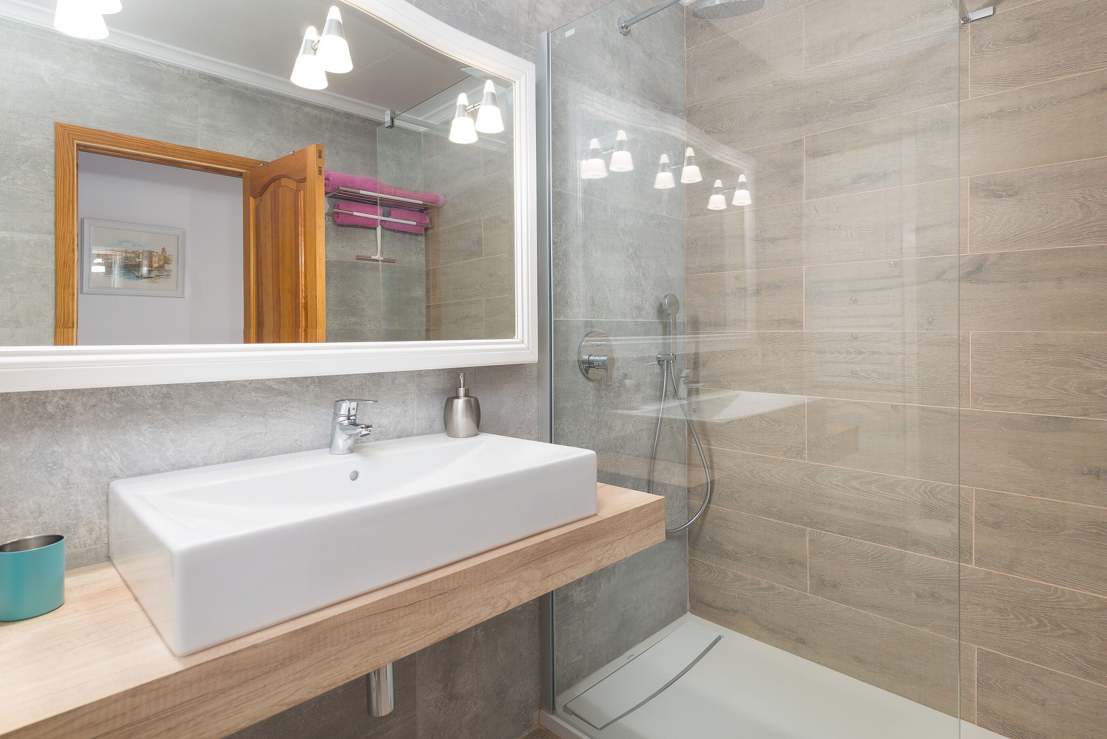 A modern bathroom with a large mirror, a white sink, and a glass shower enclosure.