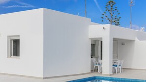 Ein modernes, weißes Gebäude mit Pool, Sitzgelegenheiten im Freien und blauem Himmel.