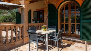 Eine Terrasse im Freien mit Tisch und Stühlen, Steinpfeilern und grünen Fensterläden.