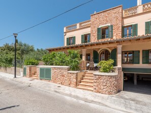 A two-story building with a stone facade, green shutters, and a covered porch with outdoor seating.
