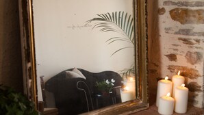 A mirror with a gold frame, a black sofa, a potted plant, and three lit candles on a stone ledge. - Il etait une fois chez moi Eugénie (Le Loroux-Bottereau)