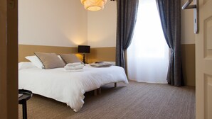A hotel room with a bed, a bedside lamp, a window with curtains, and a carpeted floor. - Il etait une fois chez moi Eugénie (Le Loroux-Bottereau)