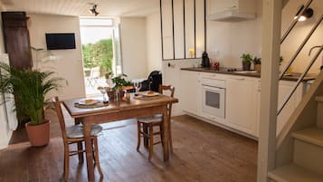 A kitchen with a wooden table, chairs, a potted plant, and a TV mounted on the wall.