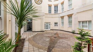 A courtyard with a circular brick pattern, a clock on the wall, and a palm tree. - Hounds Gate Court (Nottingham)