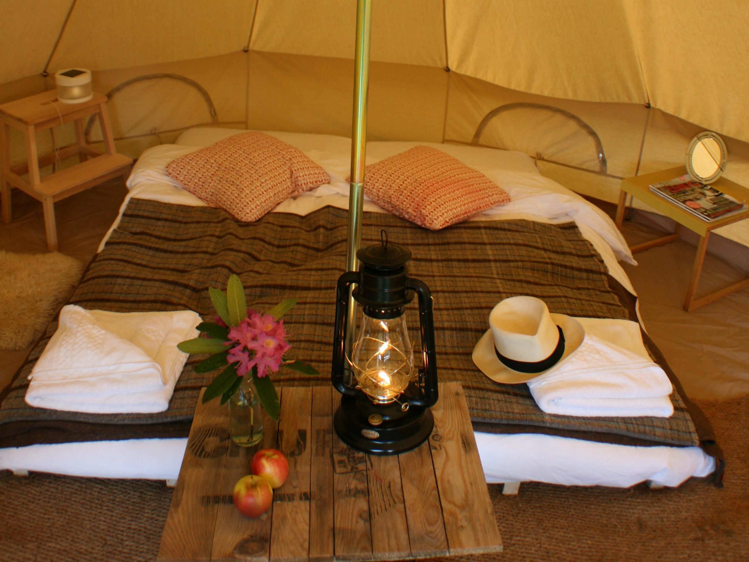 Een gezellige tent met een bed, een tafeltje met een lantaarn, appels en een vaas met bloemen.