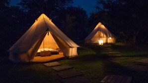 Zwei Zelte mit Innenbeleuchtung, eine Rasenfläche und ein Holzweg.