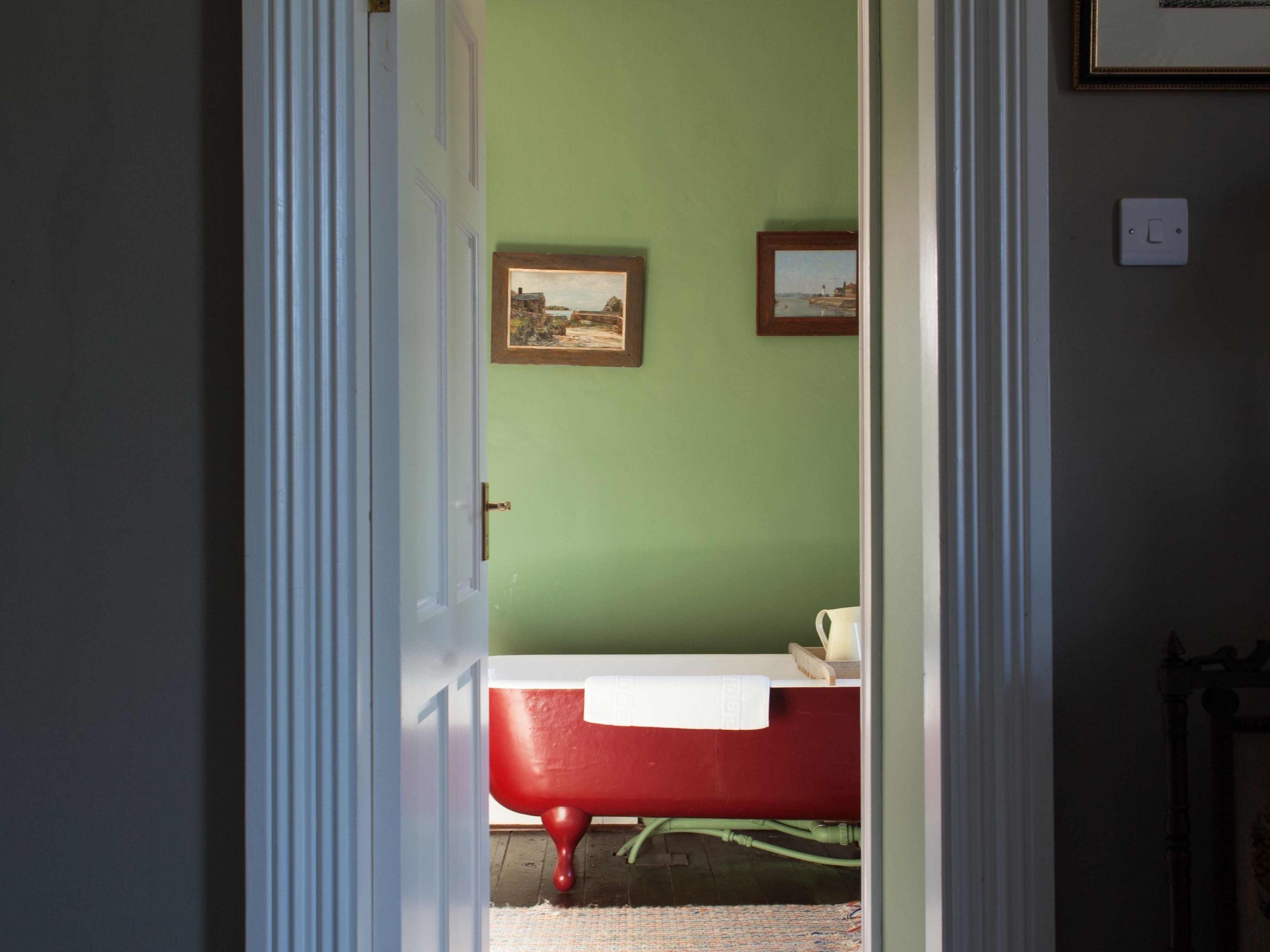 A bathroom with a red bathtub, a white sink, and two framed pictures on the wall.