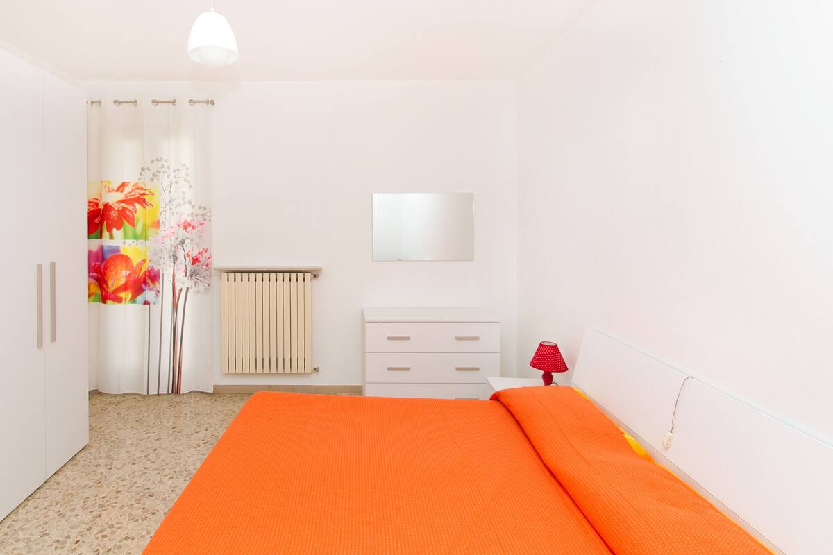 Un dormitorio con cama, armario, radiador y espejo en la pared.