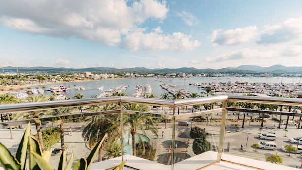 A balcony with a view of a marina, palm trees, and a parking area. - Sa Clau by Mambo (Sant Antoni de Portmany)