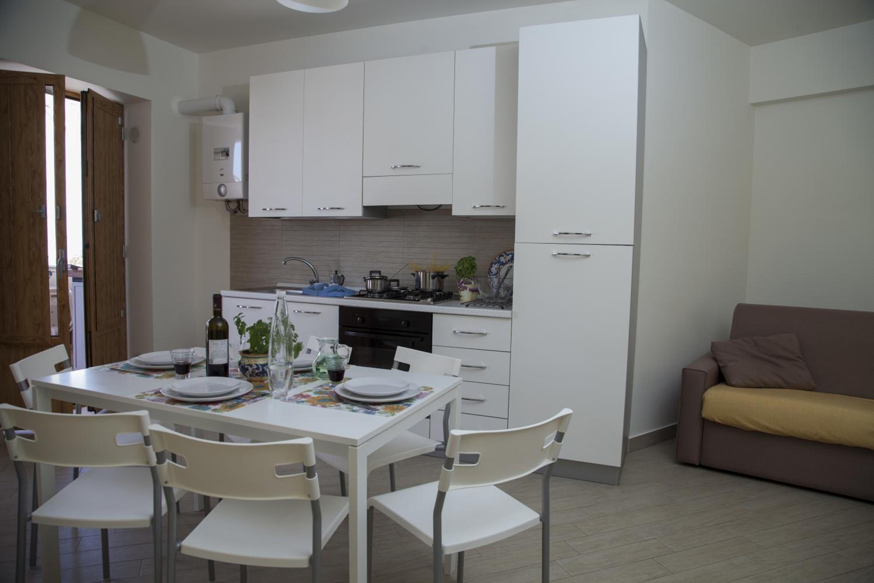 Una cucina compatta con mobili bianchi, un tavolo da pranzo con sedie, un divano e un piccolo frigorifero.