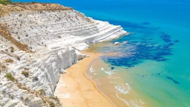 Un paysage côtier caractérisé par de hautes falaises blanches, une plage de sable et une eau d’un bleu limpide.