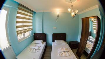 Una habitación con dos camas, una ventana con persianas, una lámpara fijada a la pared y un espejo.