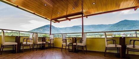 A terrace with wooden ceiling and chairs, overlooking a mountainous landscape.