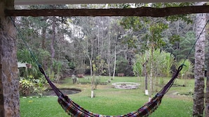 Una hamaca colgada entre árboles en un jardín exuberante con una estructura de piedra circular al fondo.