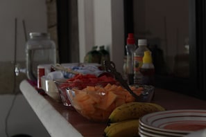 A table with various food items including a bowl of sliced fruit, a banana, and condiments.