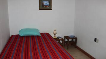 Una habitación pequeña y sencilla con una cama, una mesita de noche, una lámpara y un cuadro en la pared.
