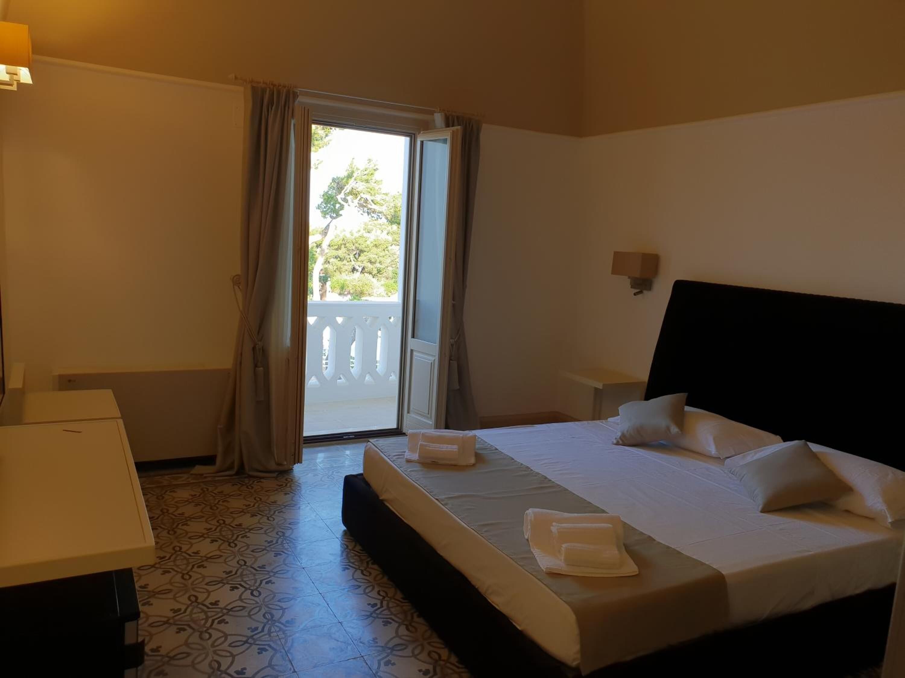 Habitació d'hotel amb llit, escriptori i finestra amb cortines.