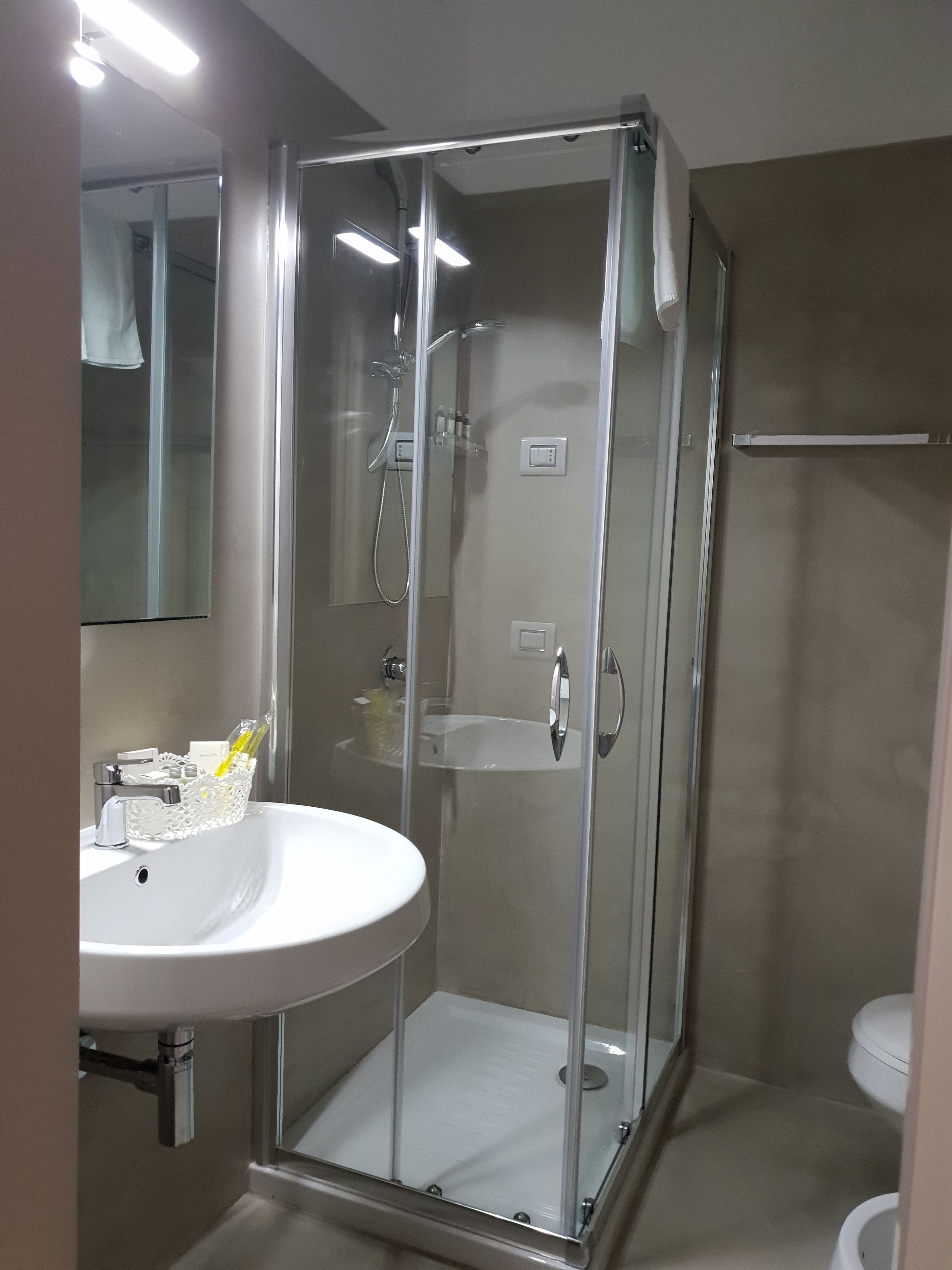 A modern bathroom with a glass-enclosed shower, a white sink with toiletries, and a mirror above the sink.